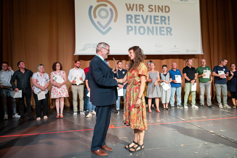 Dr. Jürgen Ude übergibt einer Preisträgerin ihre Urkunde auf der Bühne.